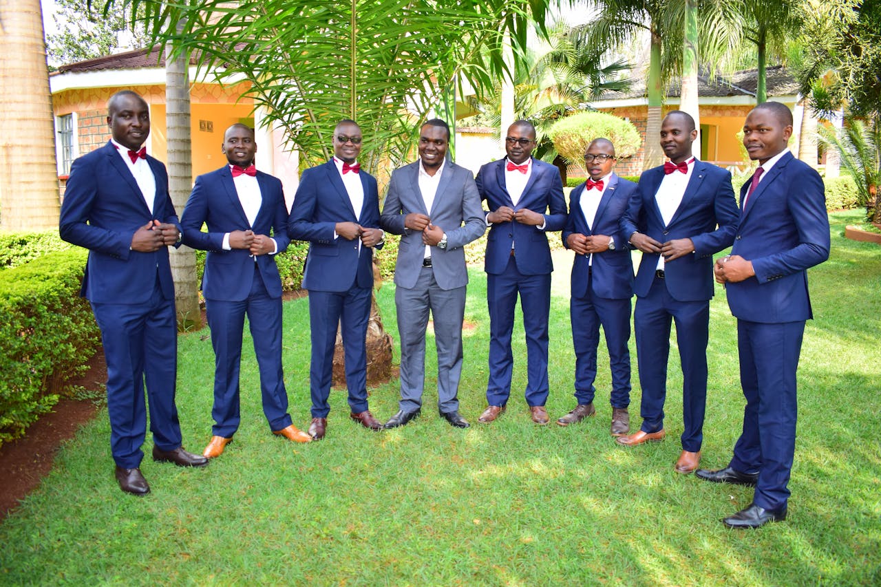 A group of men in formal suits and bow ties standing together in a garden setting.