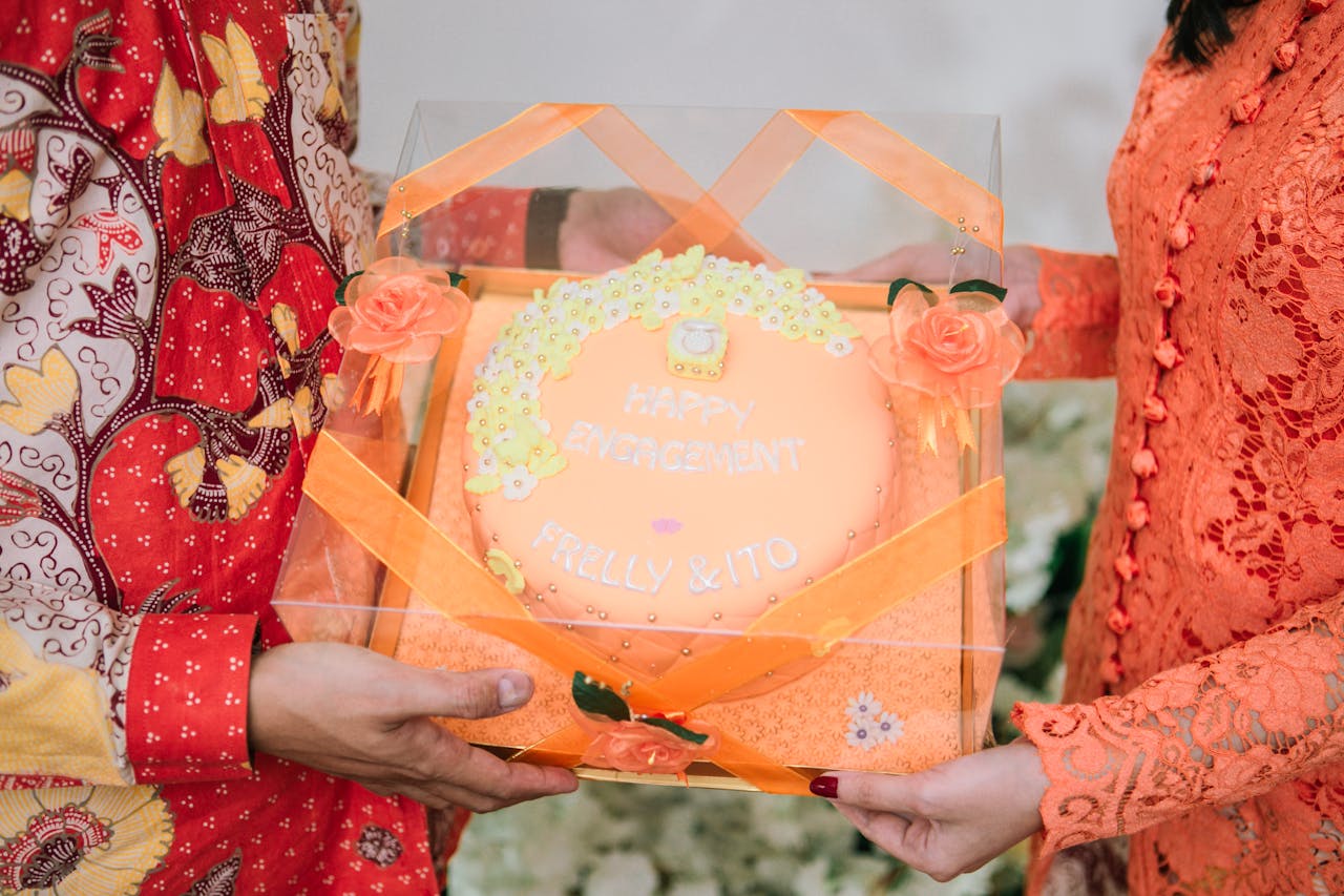 Vibrant engagement cake with floral decorations held by a couple in traditional attire.