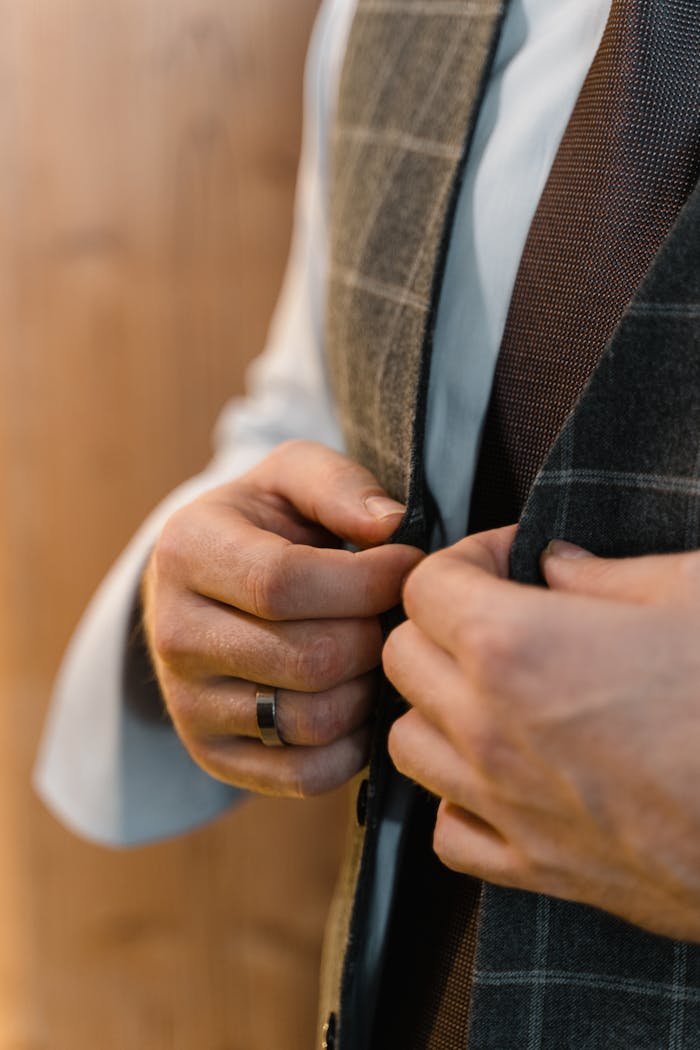 Close-up of a mans hands buttoning a stylish tailored suit, showcasing elegance and craftsmanship.