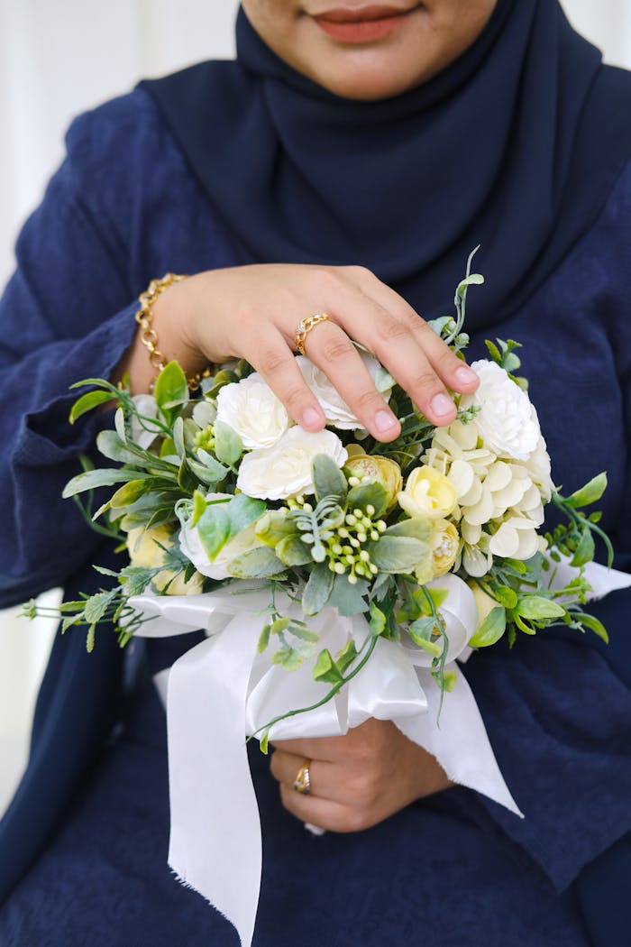 Close-up shot of a woman in a blue dress holding a delicate green and white floral bouquet.